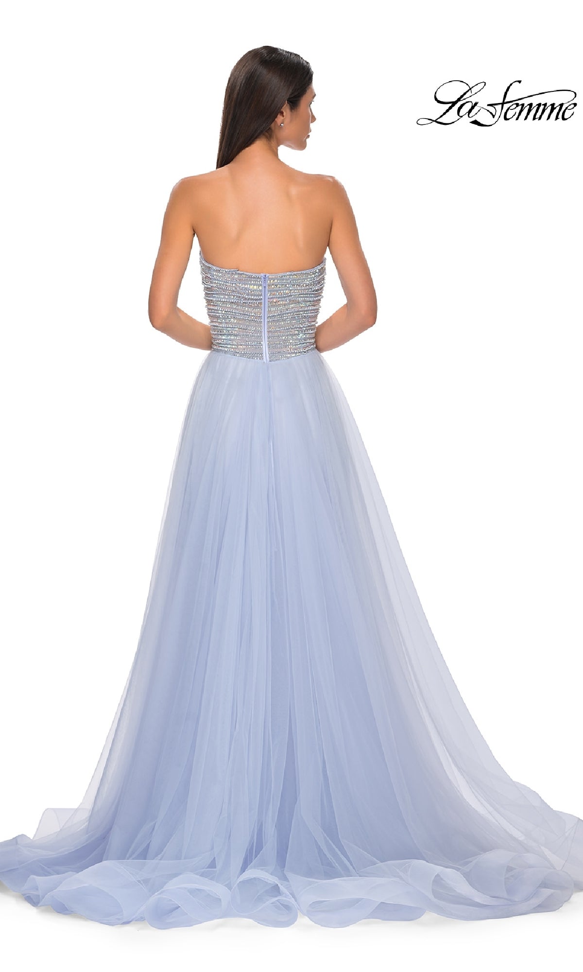 A woman in the Strapless Long Prom Ball Gown La Femme 32875, featuring a beaded bodice and flowing tulle skirt, stands with her back to the camera.